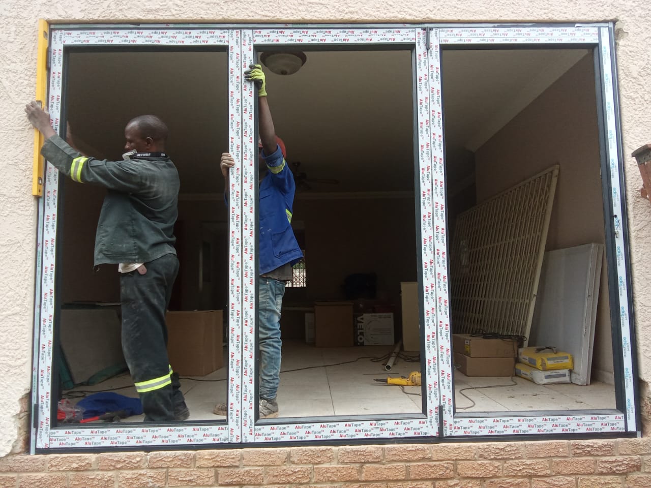 Workers installing a large aluminium sliding door frame with protective tape still on