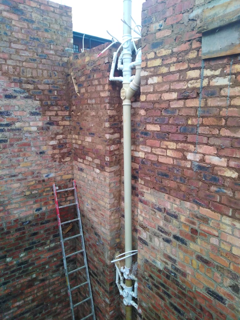 Brick wall with plumbing pipework being built in around wet services