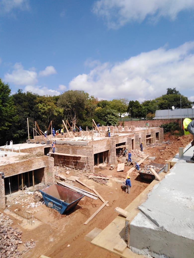 Wide view of a brick complex development under construction with workers on multiple units