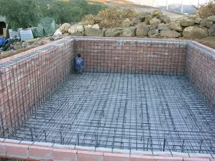 Freeform swimming pool under construction with curved reinforced walls and piping installed